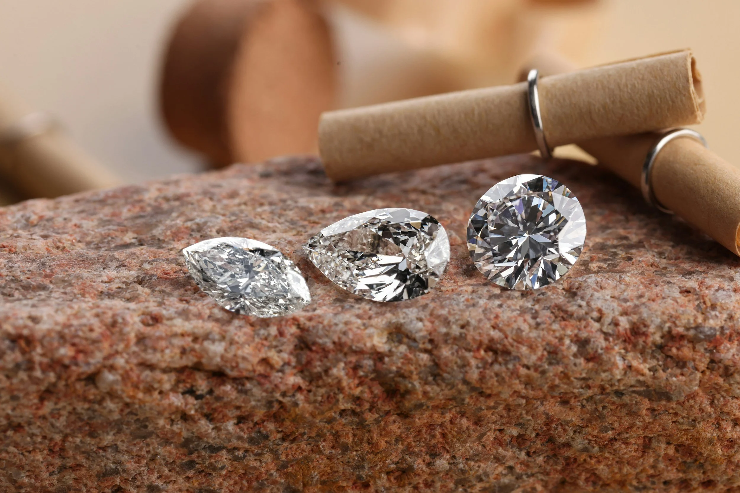 Three large, sparkling diamonds on a rough, textured granite surface with a small roller on the background.