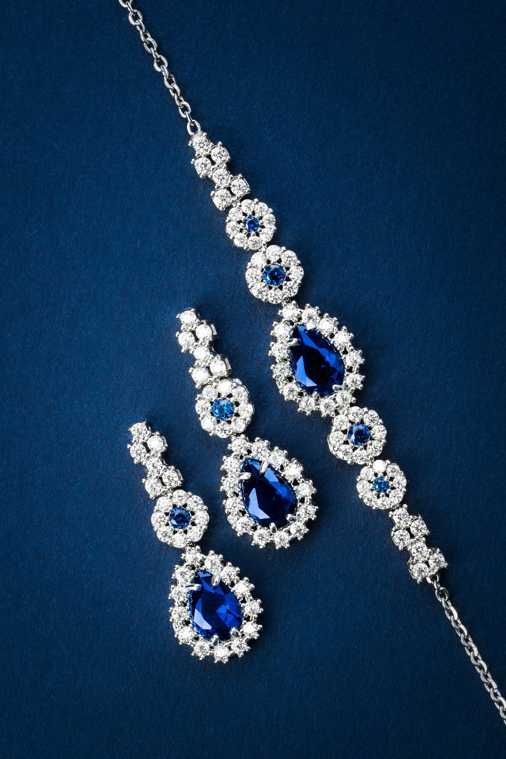 A silver necklace with blue and clear gemstones arranged in a cascading pattern, set against a dark blue background.