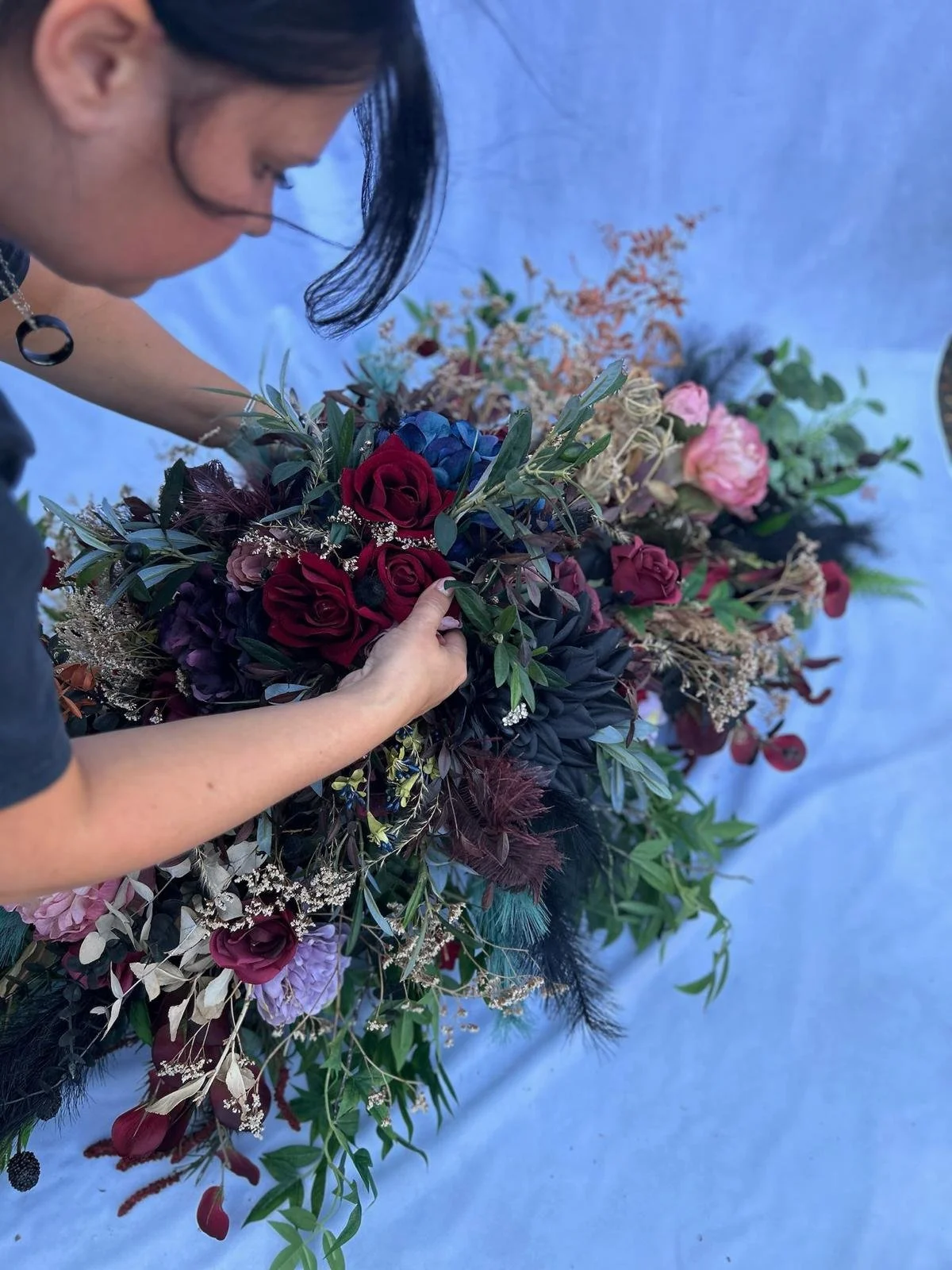 A person arranging a large, colorful floral bouquet with various flowers and greenery on a blue surface.