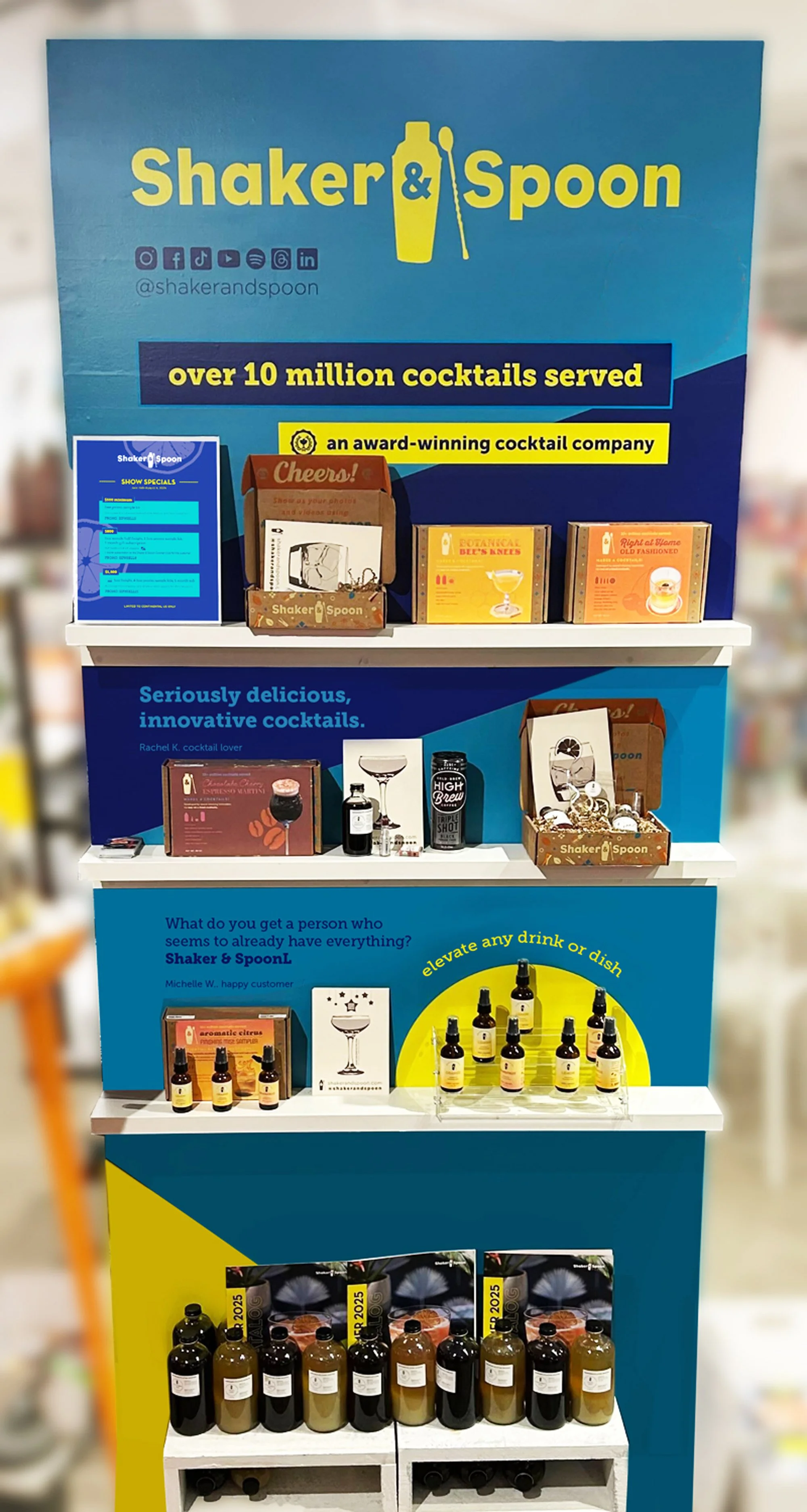 Display shelf featuring various cocktail ingredients, mixers, and accessories for making alcoholic drinks at Shaker & Spoon.