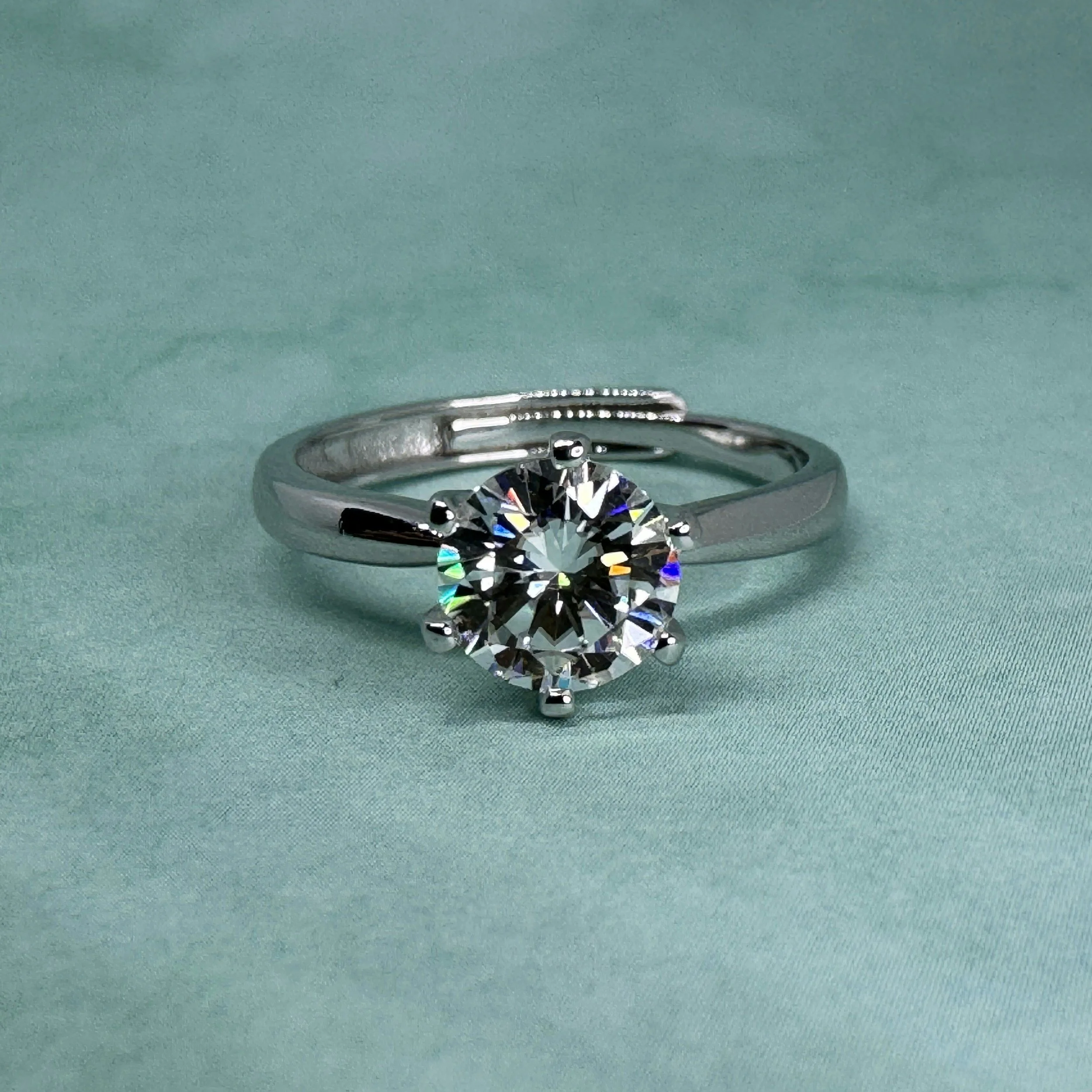 Close-up of a diamond engagement ring with a large round-cut diamond on a teal fabric background.