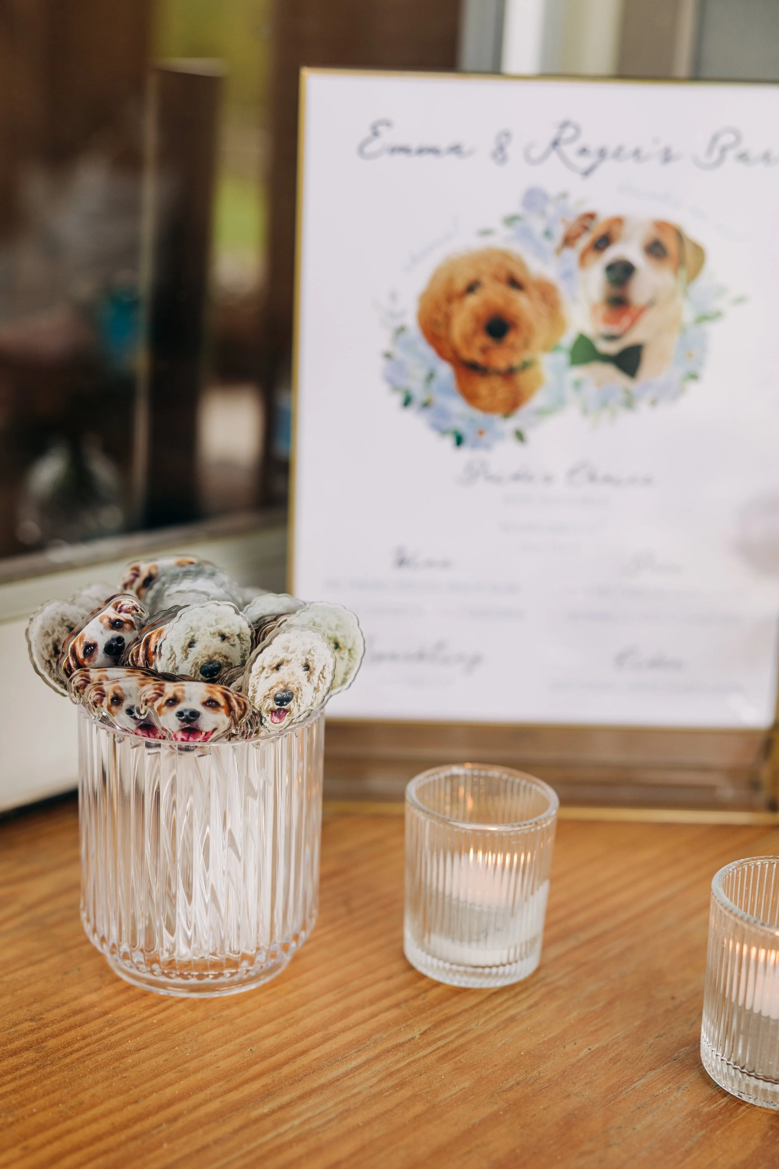 Clear glass vase with dog-printed cupcake toppers, and a blurred sign in the background featuring two dog photos and cursive text.