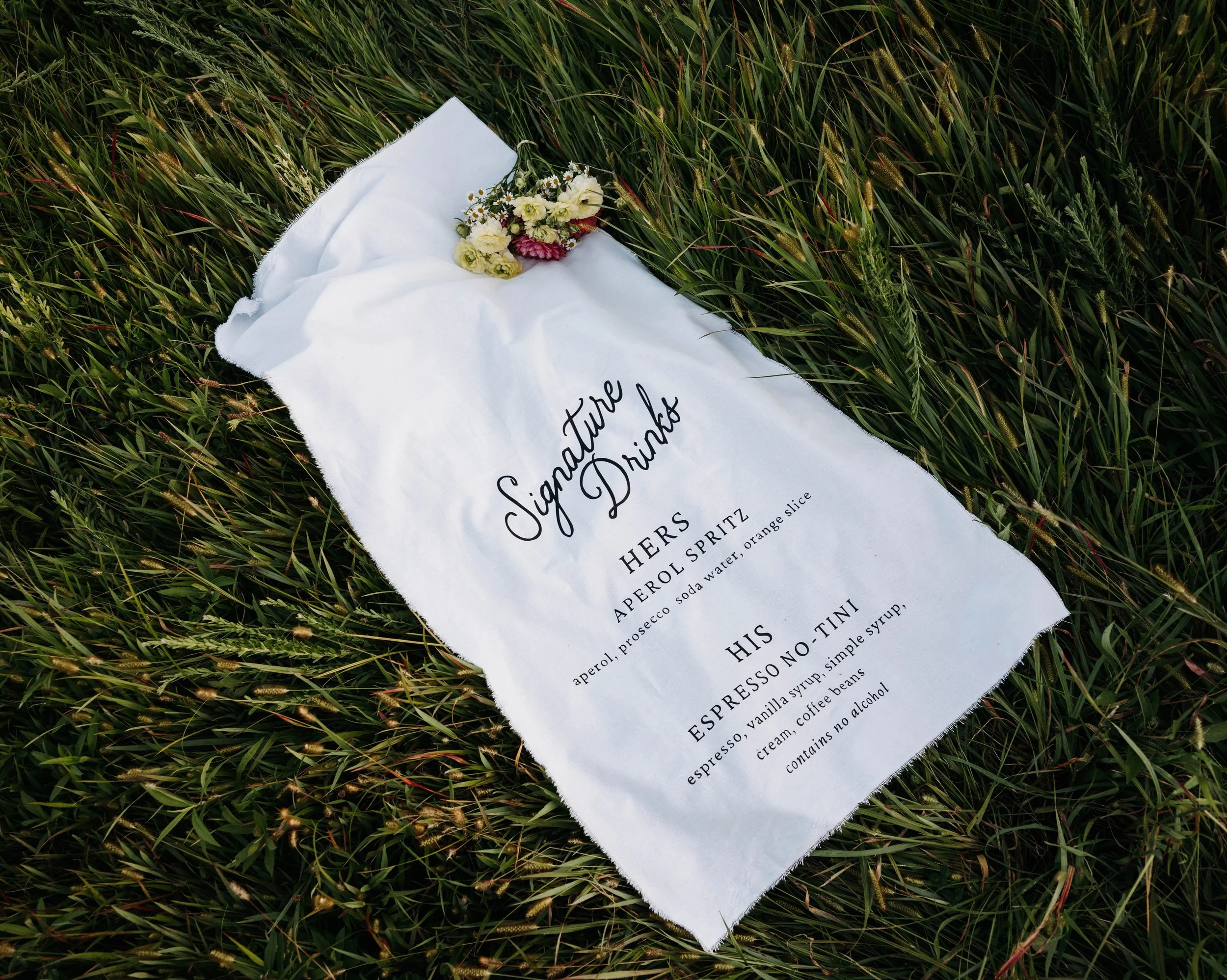 Wedding bouquet and a white cloth with black text on a grassy field.