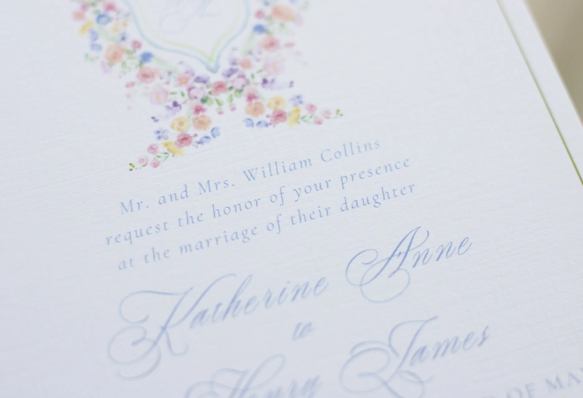 Close-up of a wedding invitation with floral design at the top and blue cursive and serif text, mentioning Mr. and Mrs. William Collins and a wedding celebration.