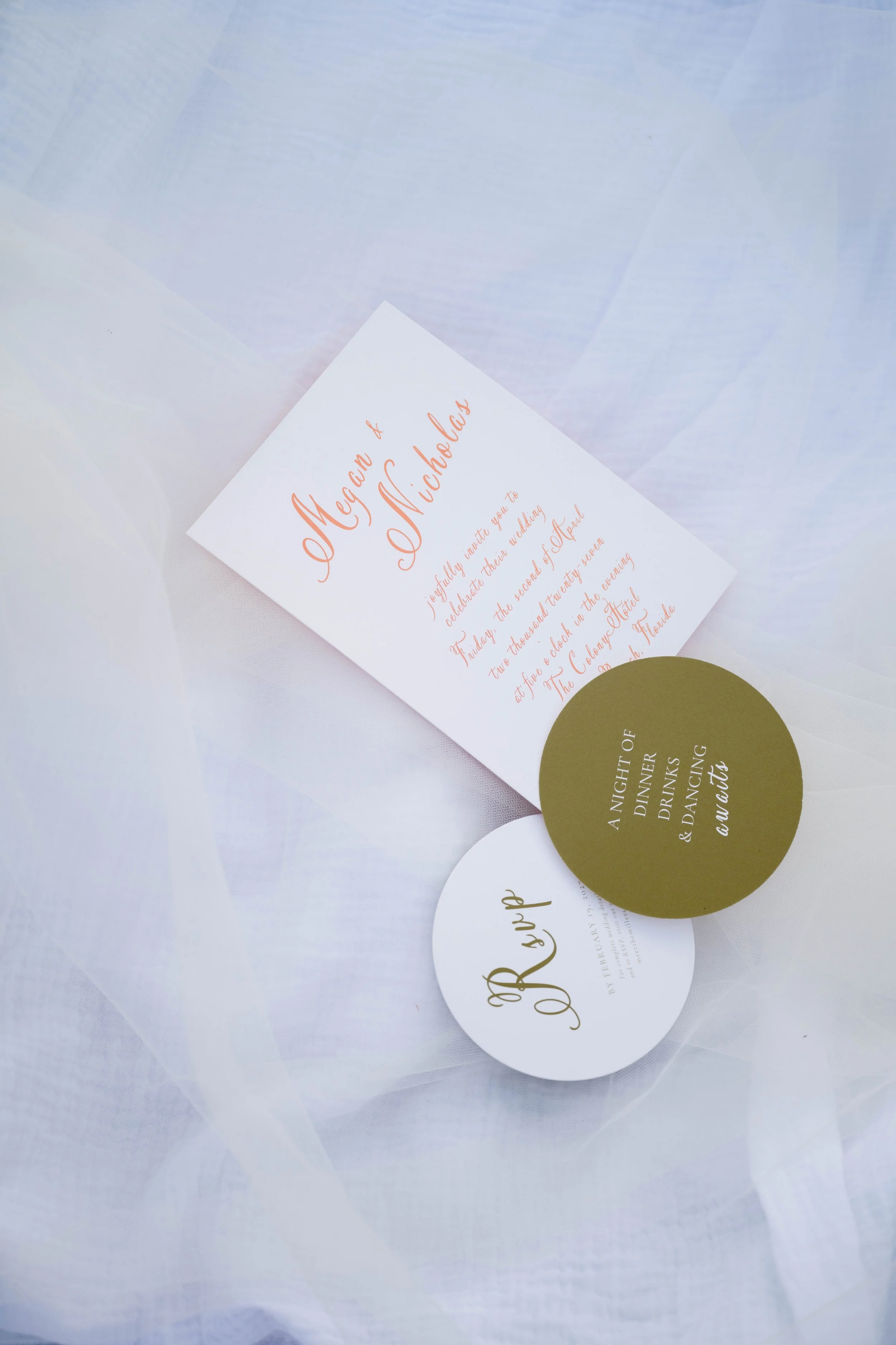 Elegant wedding invitation cards with gold and peach script on white and gold backgrounds, arranged on a white fabric surface.