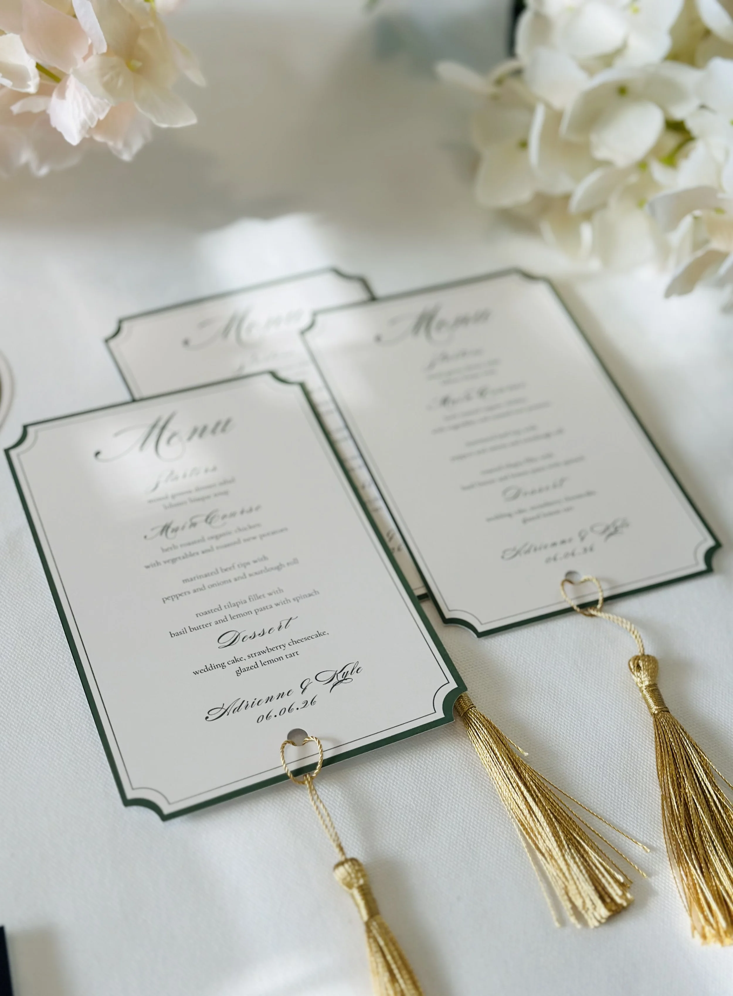 Wedding menu cards with gold tassels, surrounded by white flowers.