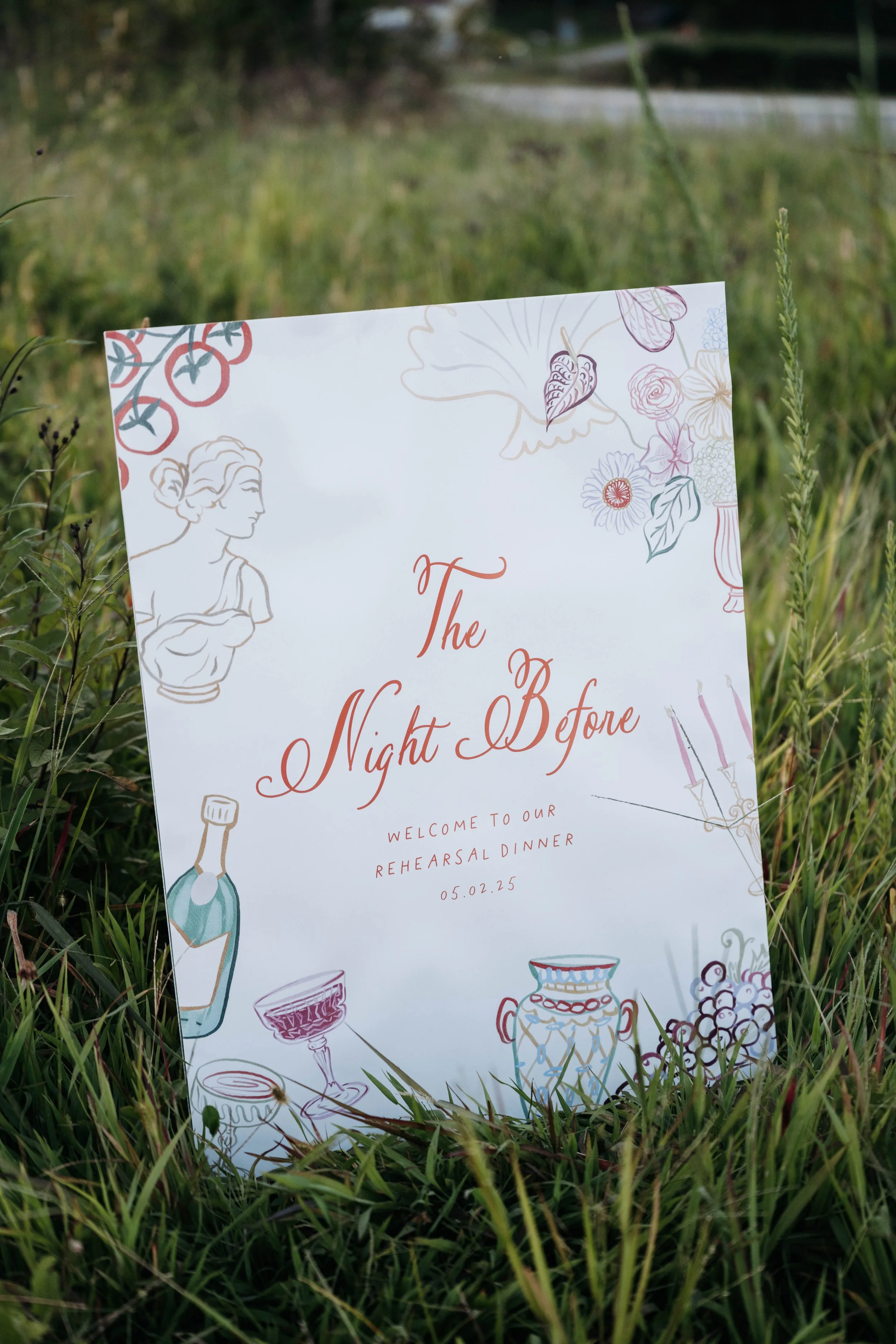 A wedding or event invitation card placed among green grass outdoors, featuring floral and decorative illustrations, with the date 05.02.25.