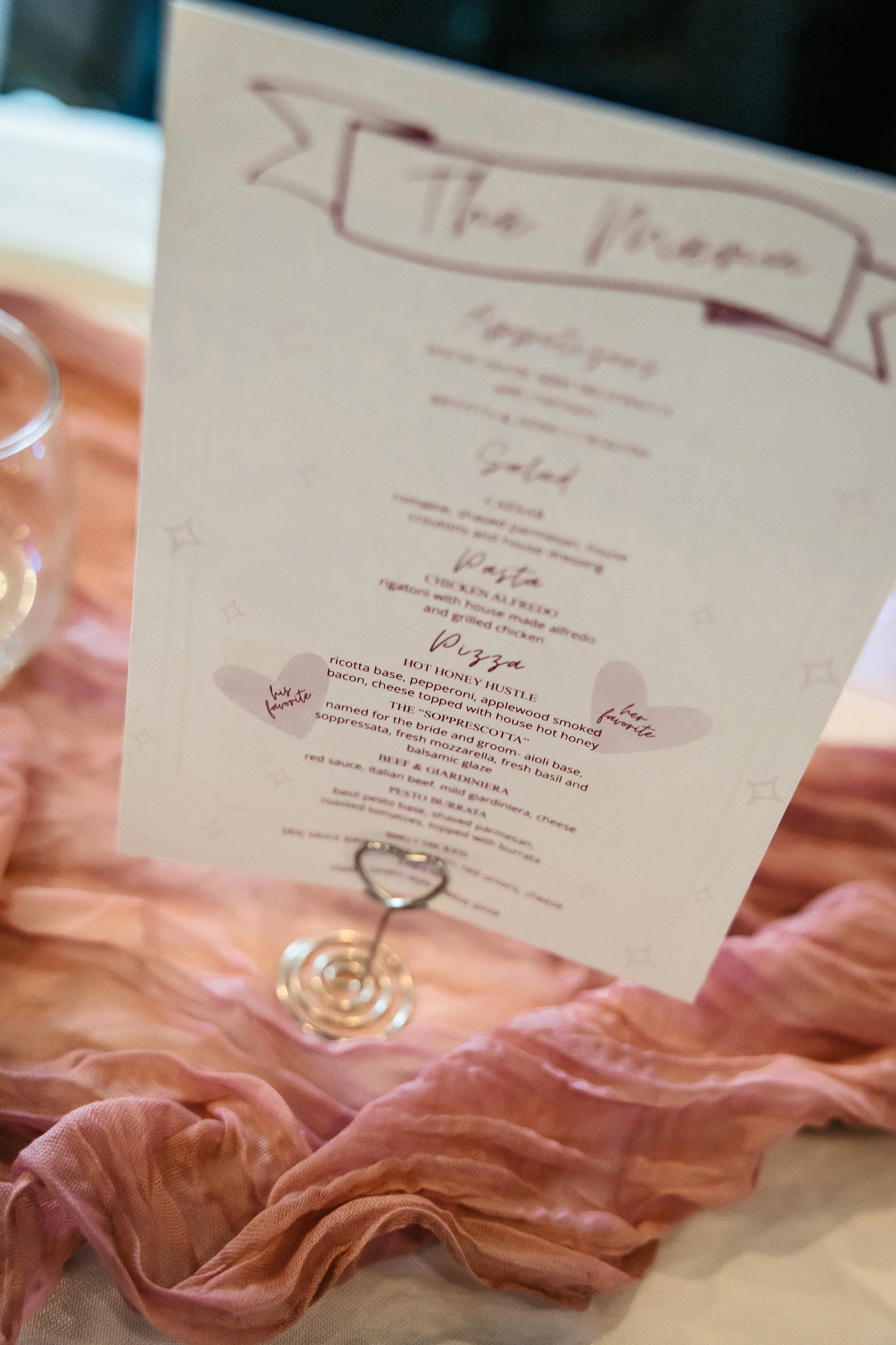 Close-up of a pink bridal or fancy dress with a paper menu or program attached, decorated with a heart-shaped paperclip, in a soft pink setting.