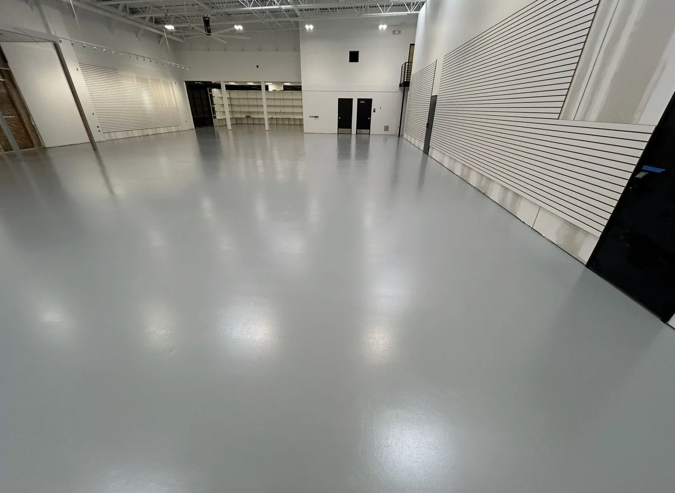 Empty indoor commercial space with smooth gray floor, white walls, and ceiling, featuring some wooden and slat wall accents.
