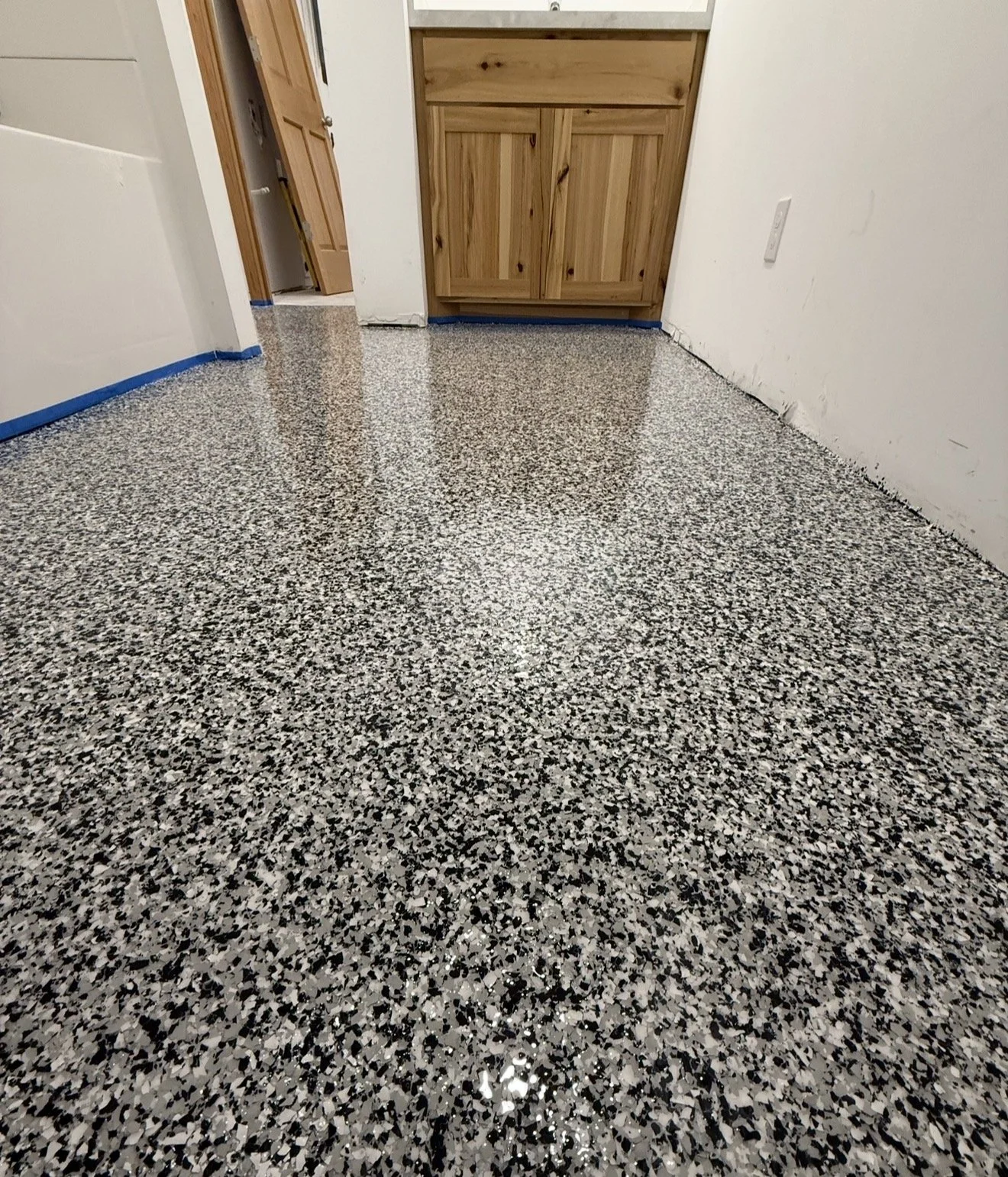 Interior room with speckled black, white, and gray epoxy floor, white walls, wooden cabinets, and an open door.