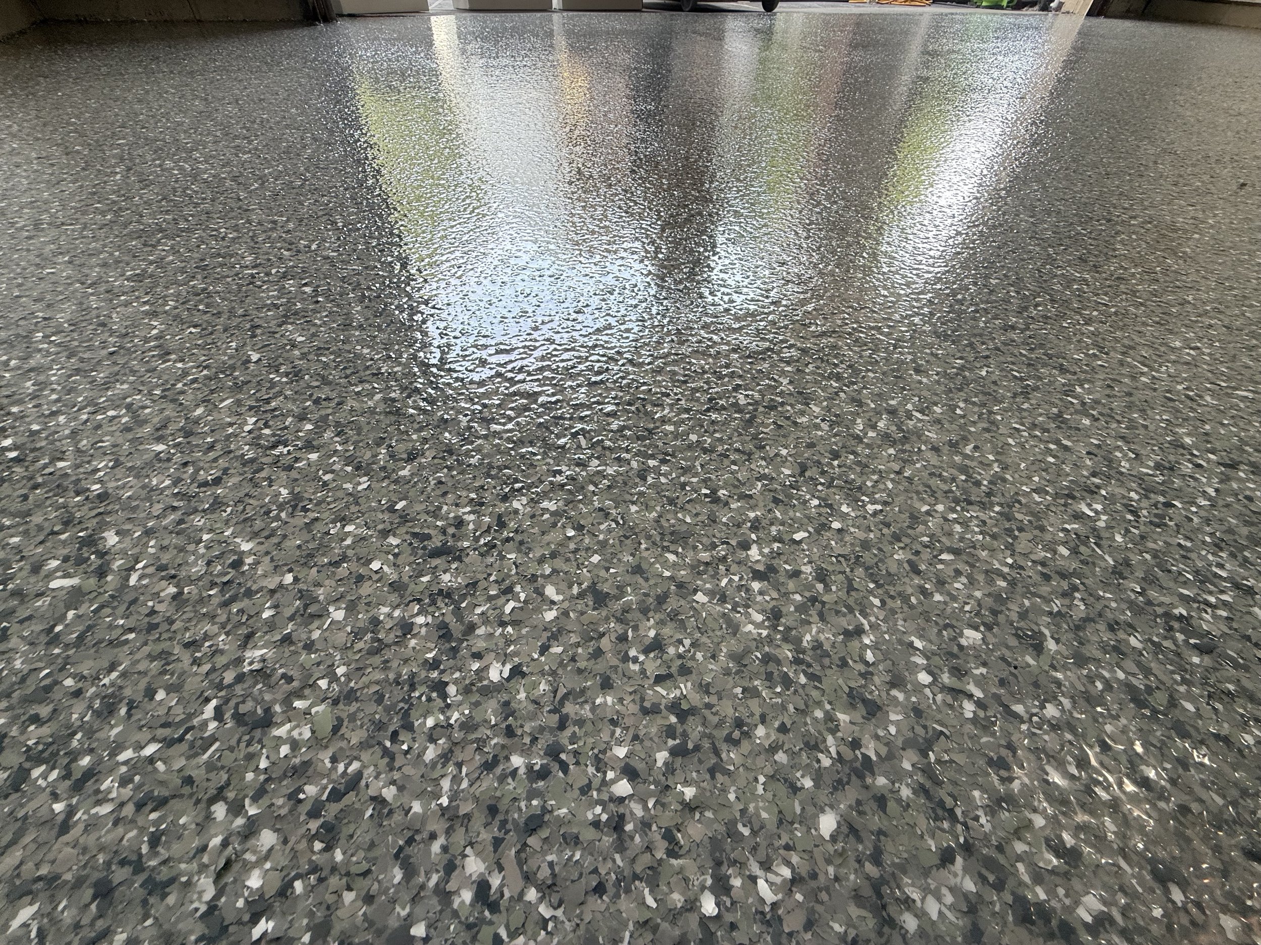 Shiny polished epoxy floor with scattered gray, black, and white flecks, reflecting natural light from windows.