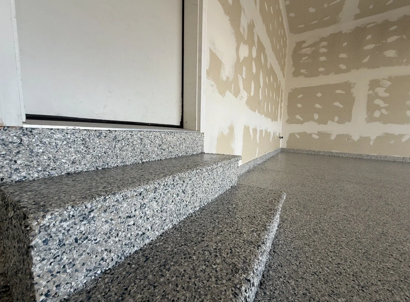 Interior of a garage with a speckled gray granite step and floor, unfinished drywall walls, and a sliding door.