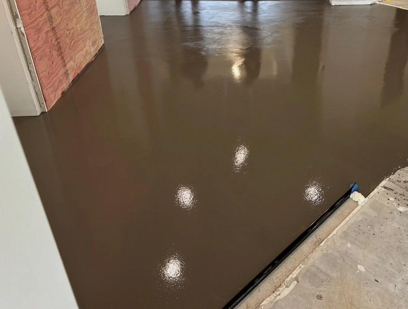 Freshly poured brown concrete flooring in an unfinished room with construction materials and partially finished walls.