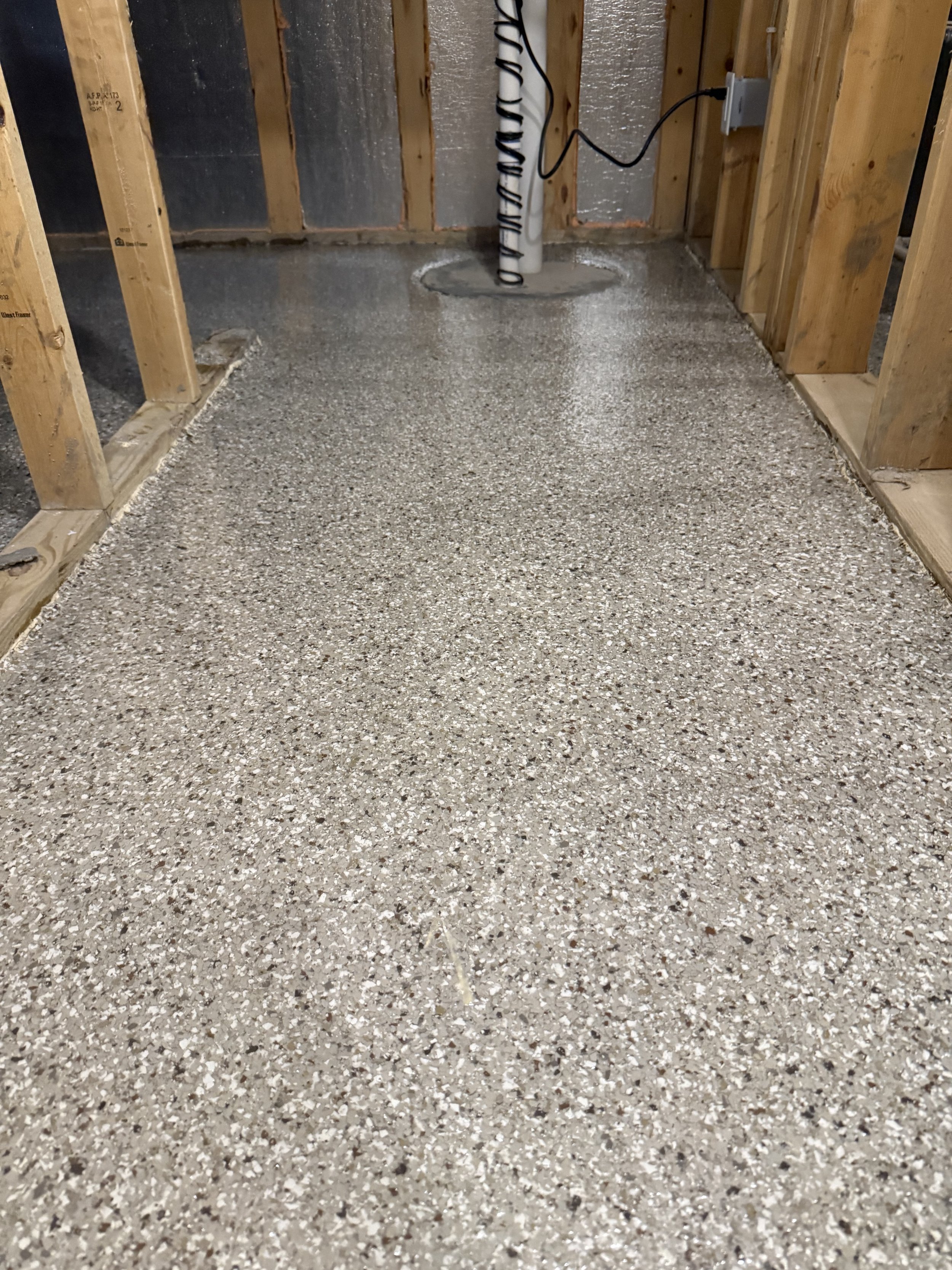 unfinished room with exposed wooden framing and a newly poured speckled epoxy concrete floor.
