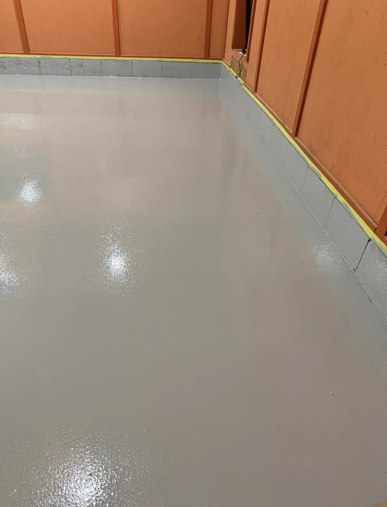 Freshly epoxied concrete floor in a room with unfinished drywall and electrical outlets along the wall.