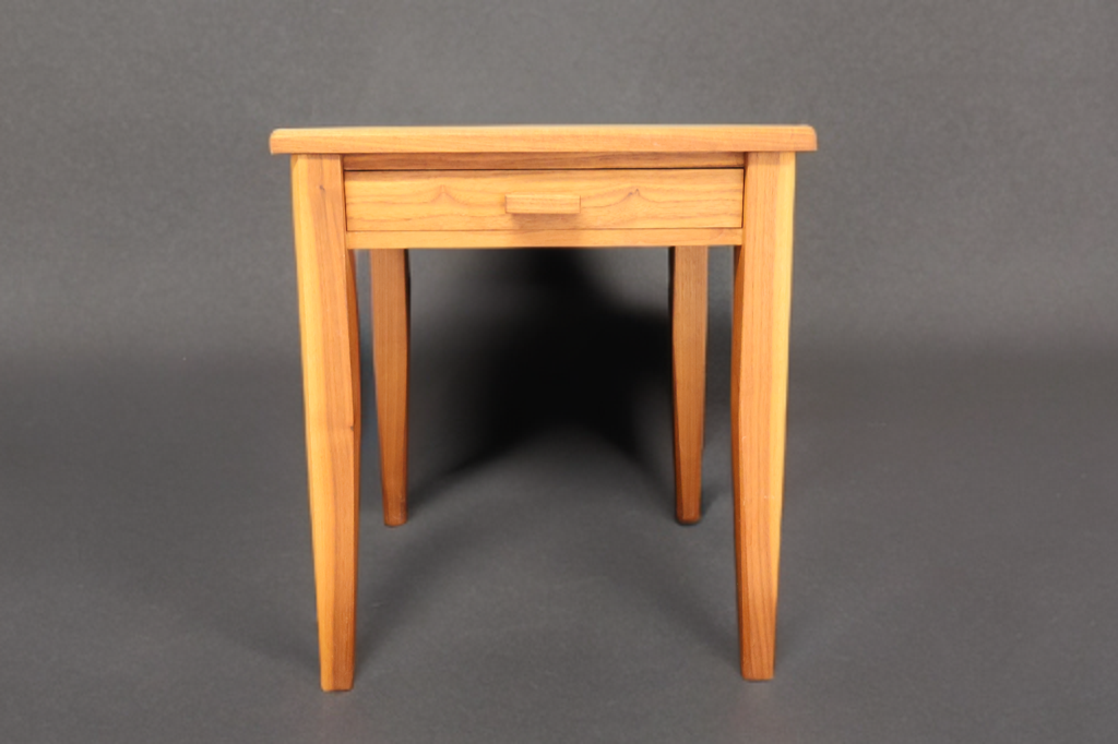Small wooden side table with a drawer, set against a dark background.