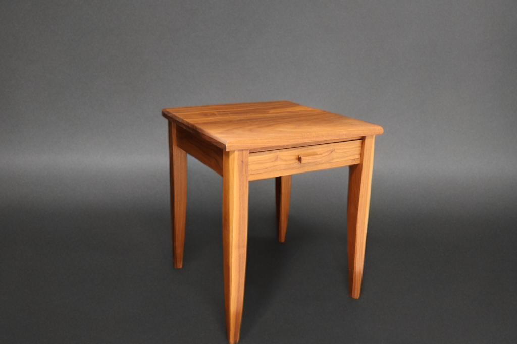 A wooden side table with a drawer against a gray background.