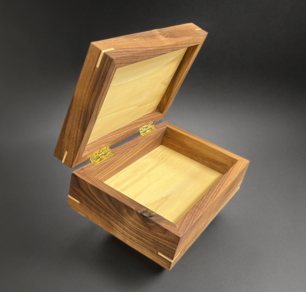 Open wooden jewelry box with a dark exterior and a lighter interior, salt and pepper wood grain, on a black surface.