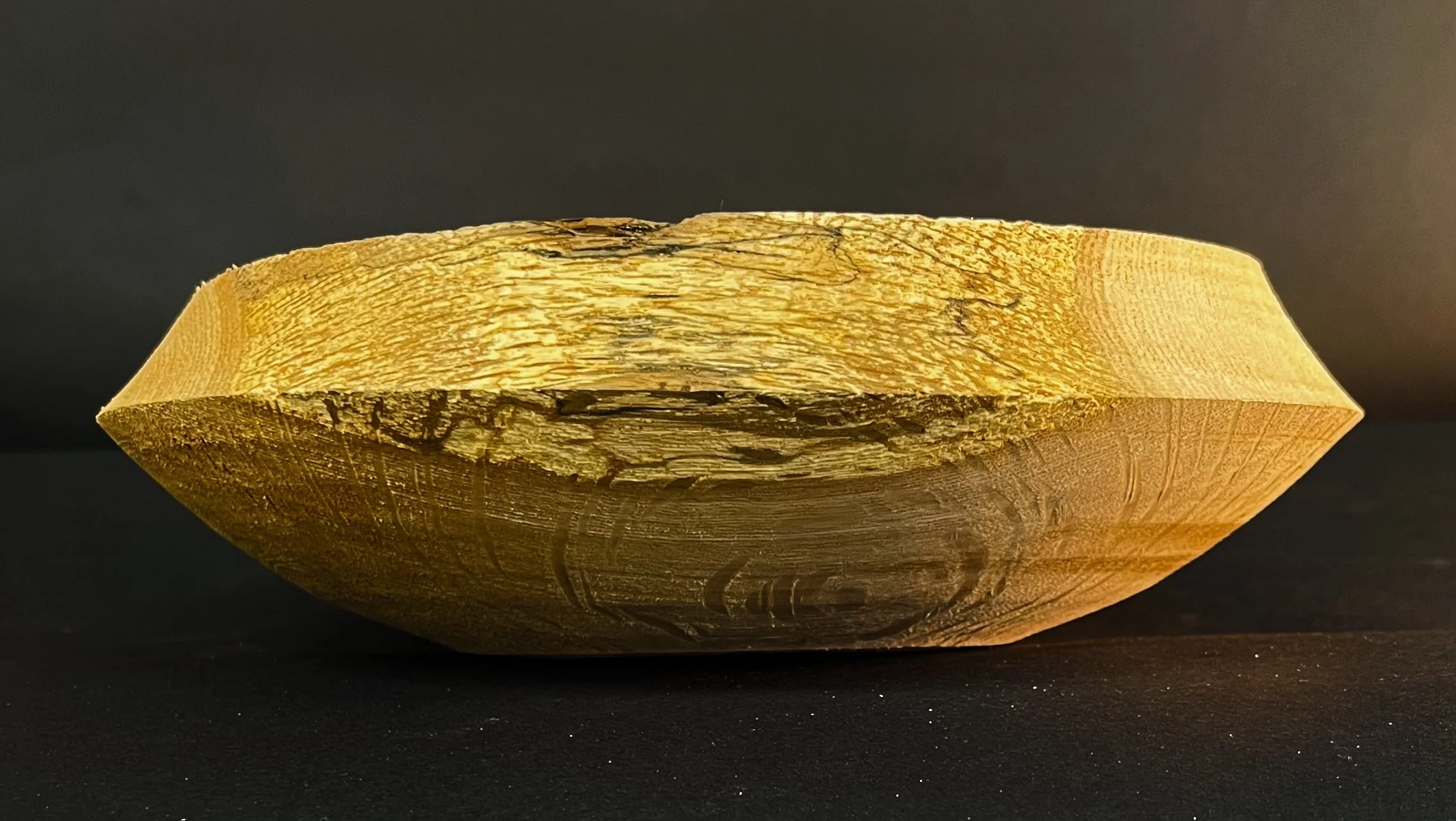 A close-up of a wooden bowl with a smooth, polished surface, showing natural wood grain and cracks, set against a black background.