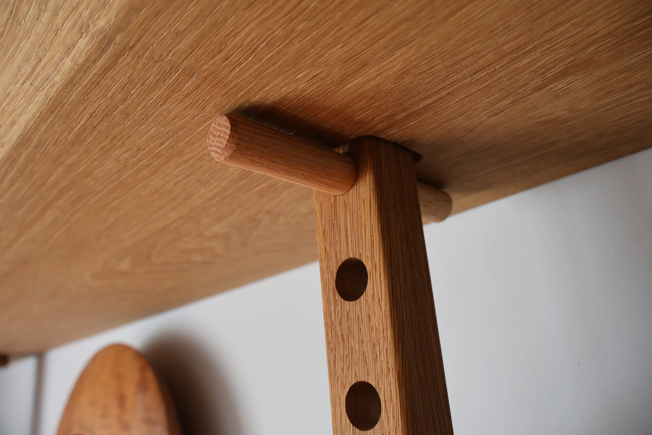 Close-up of a wooden coat hook attached to a wooden surface with a rounded end and holes for screws.