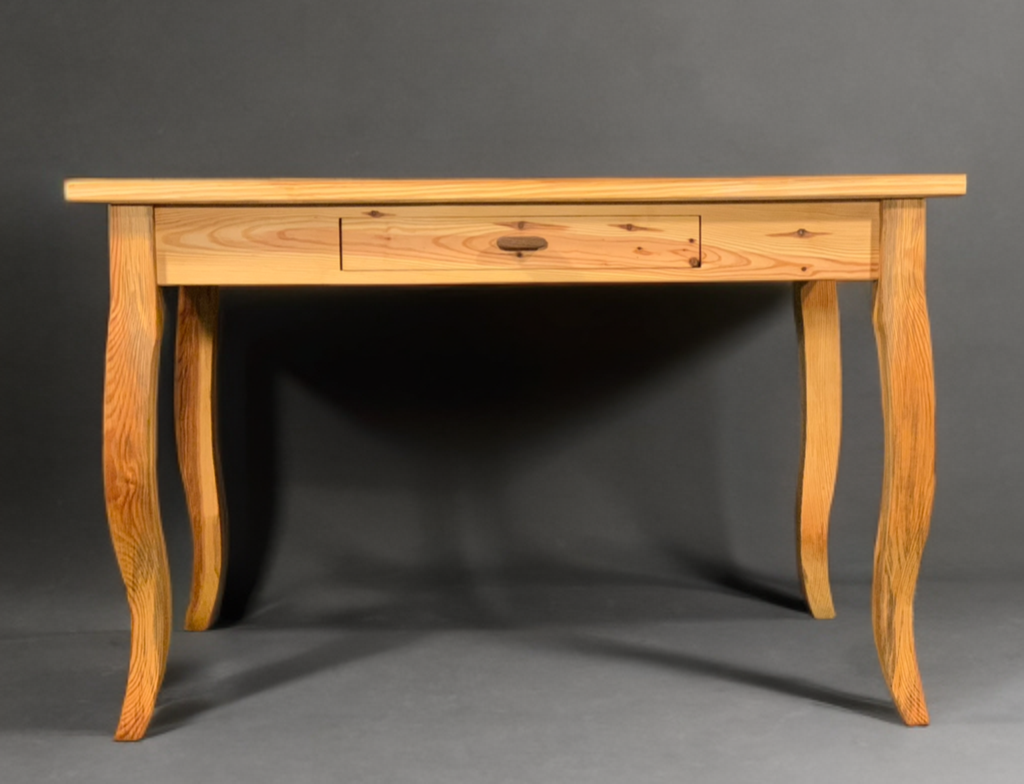 Wooden desk with four curved legs and a small drawer, set against a dark background.