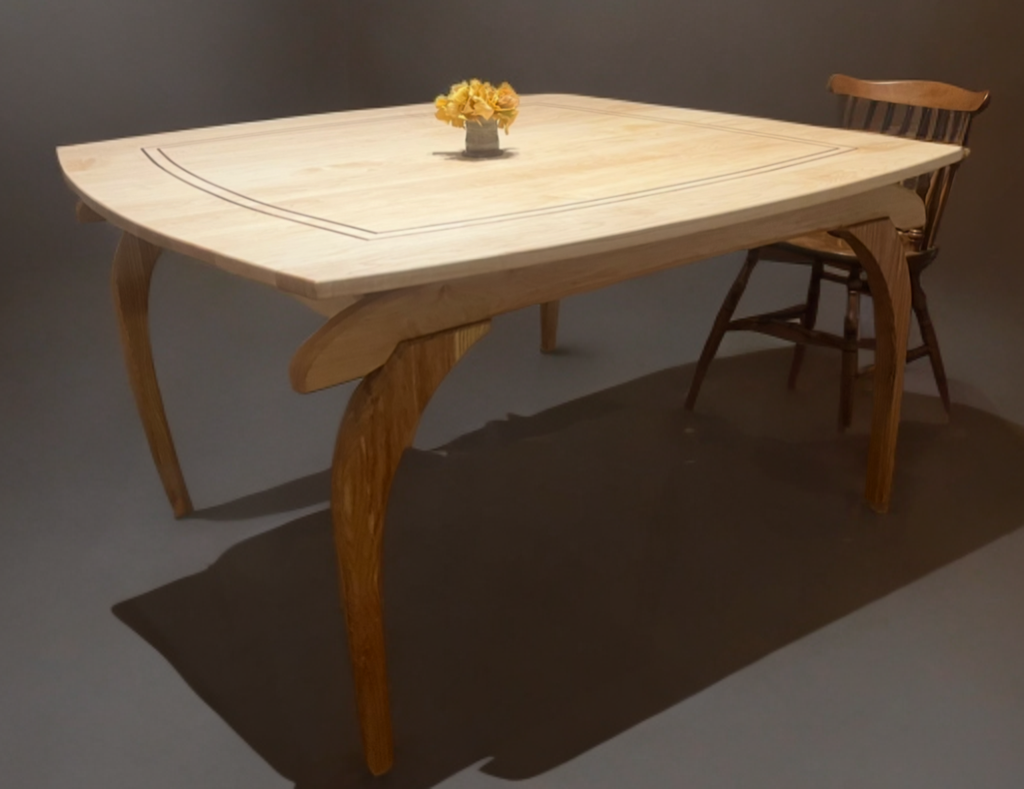 A wooden dining table with a light finish, a decorative inlay pattern around the edge, and curved legs. There is a small flower arrangement in a vase at the center, and a wooden chair with a slatted backrest positioned next to the table.