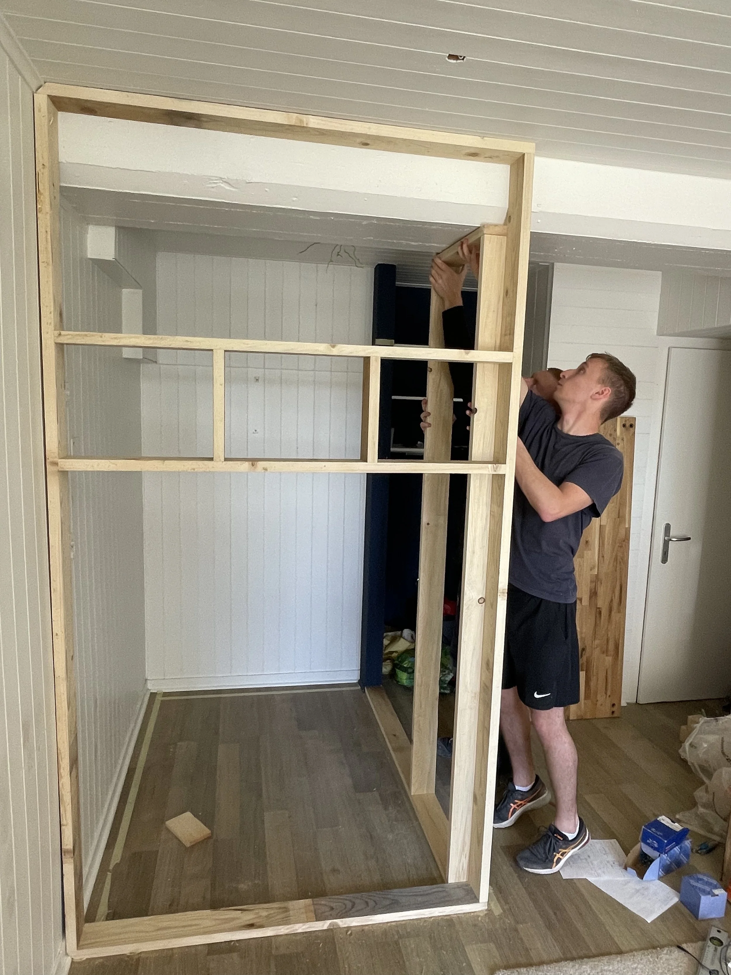 Un homme en train de construire une cloison en bois dans une pièce intérieure.