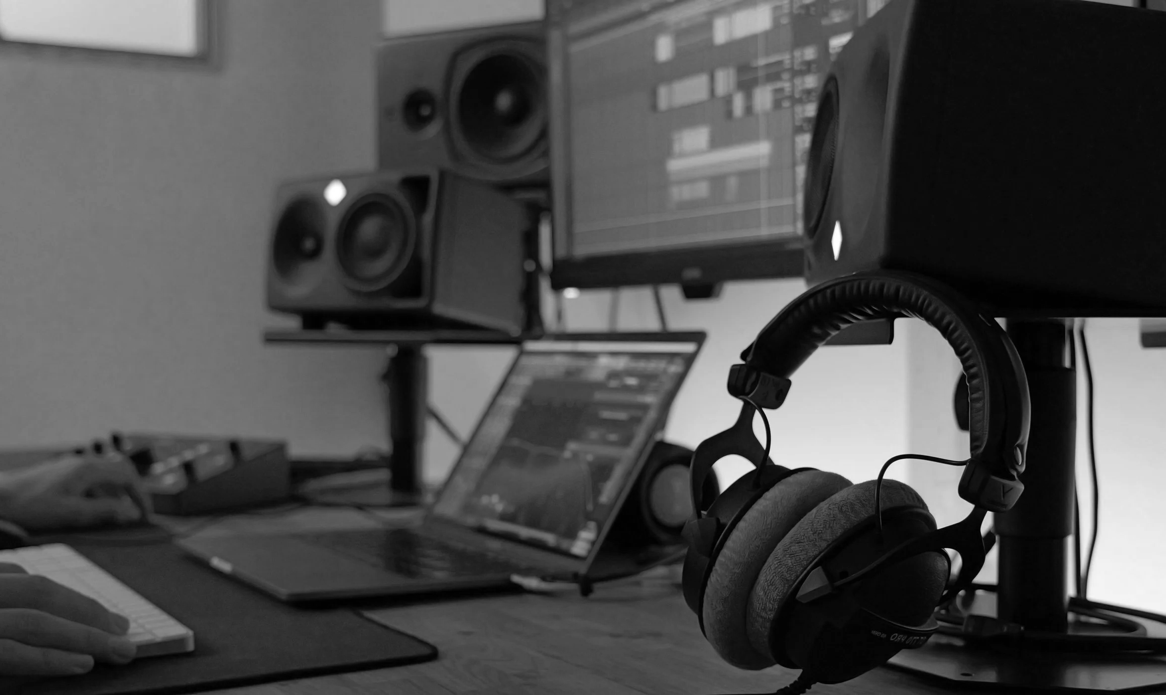 Configuration d'un poste de travail avec un ordinateur portable, un moniteur, des écouteurs autour du moniteur, et un micro connecté, dans un environnement de studio ou de bureau, en noir et blanc.