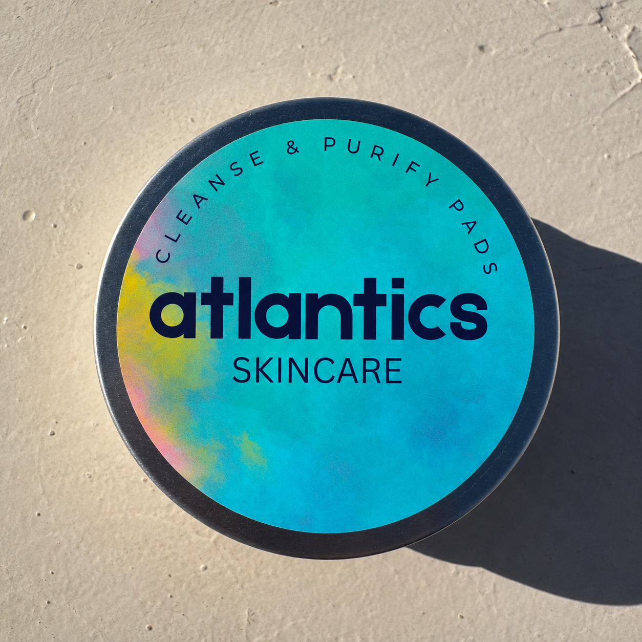 A round container of Atlantis Skincare with a colorful, holographic label on a beige surface, casting a shadow.