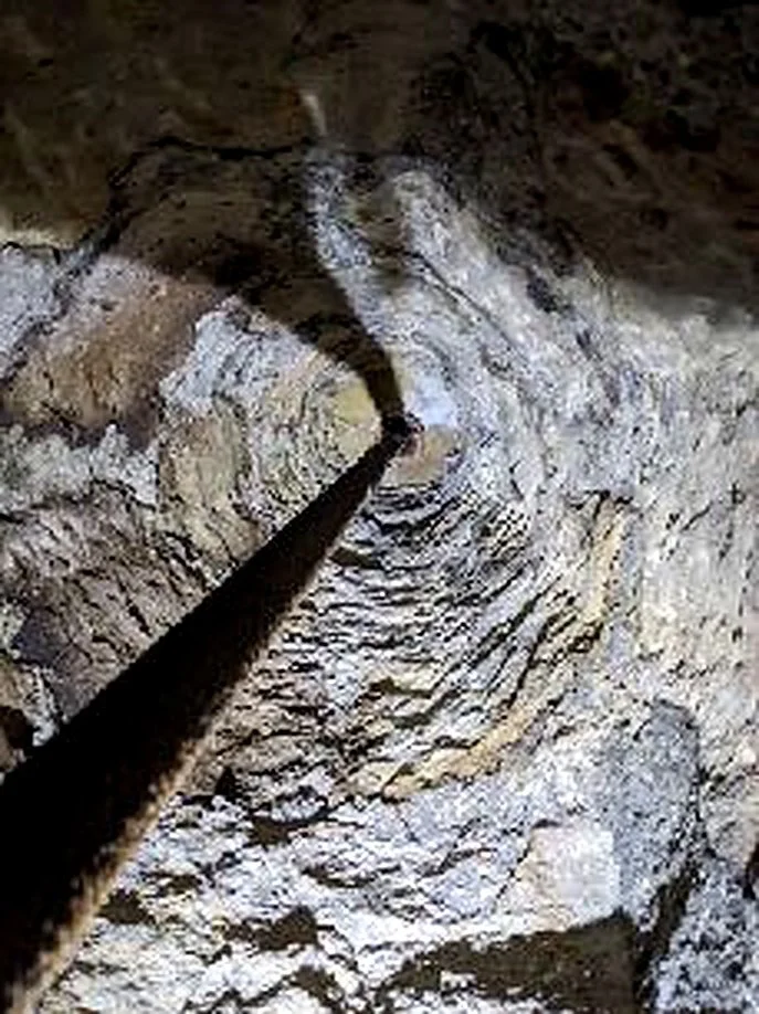 Looking up inside a deep, rocky cave or mine shaft with a black pole or pipe extending downward into the dark.