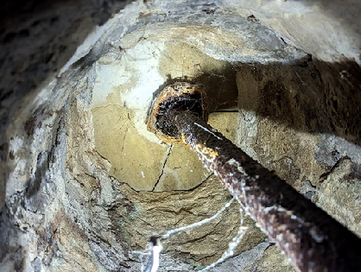 A close-up view of a metal pipe inside a stone or concrete wall, with some wires or pipes attached to it.