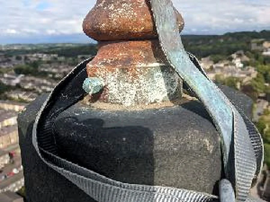 Close-up of a metal water tower or antenna on top of a building, with a scenic cityscape and rolling hills in the background.