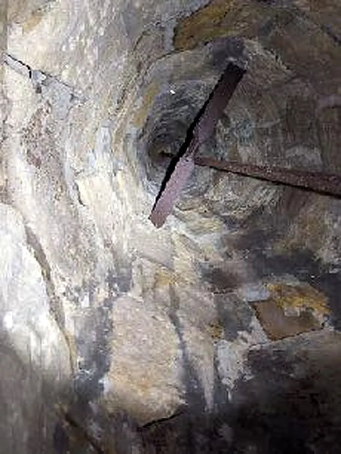 A vertical, narrow well in a rocky environment with rusty metal supports.