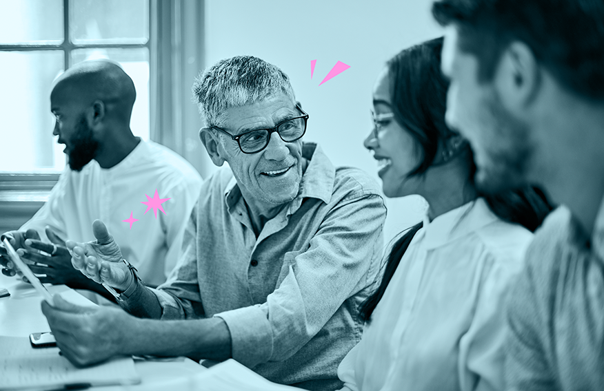 A diverse group of people in a discussion in a bright room, with a man showing something on a mobile device to others.