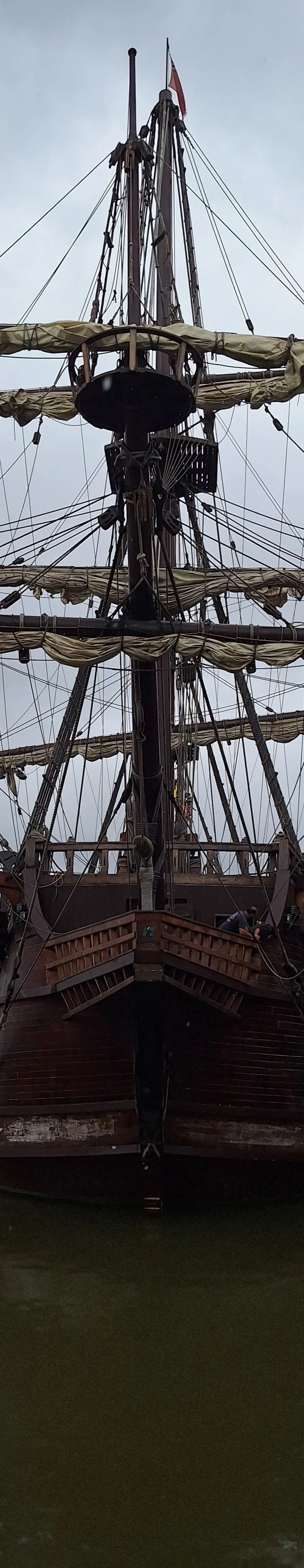 Bow of a tall wooden sailing ship, masts and rigging visible, with a flag flying from the main mast. Heritage imagery for AbeySea's Charter.