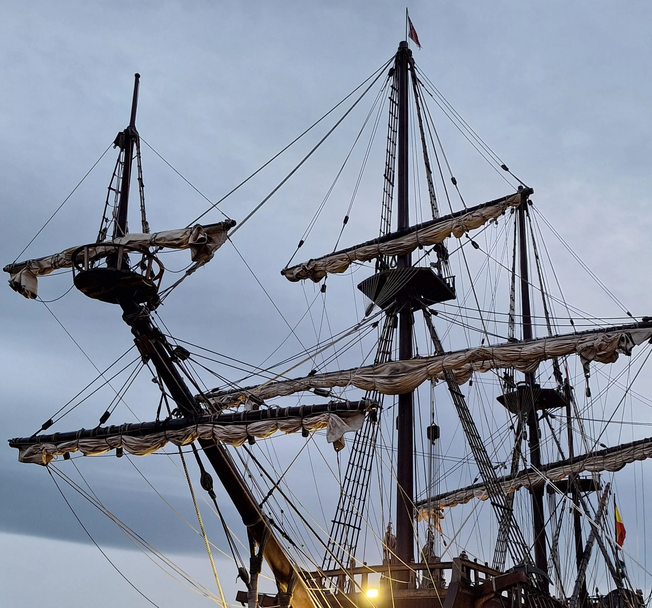 Masts and rigging of a tall ship silhouetted against a cloudy sky near sunset. Maritime heritage imagery for AbeySea's Charter and Chandlery