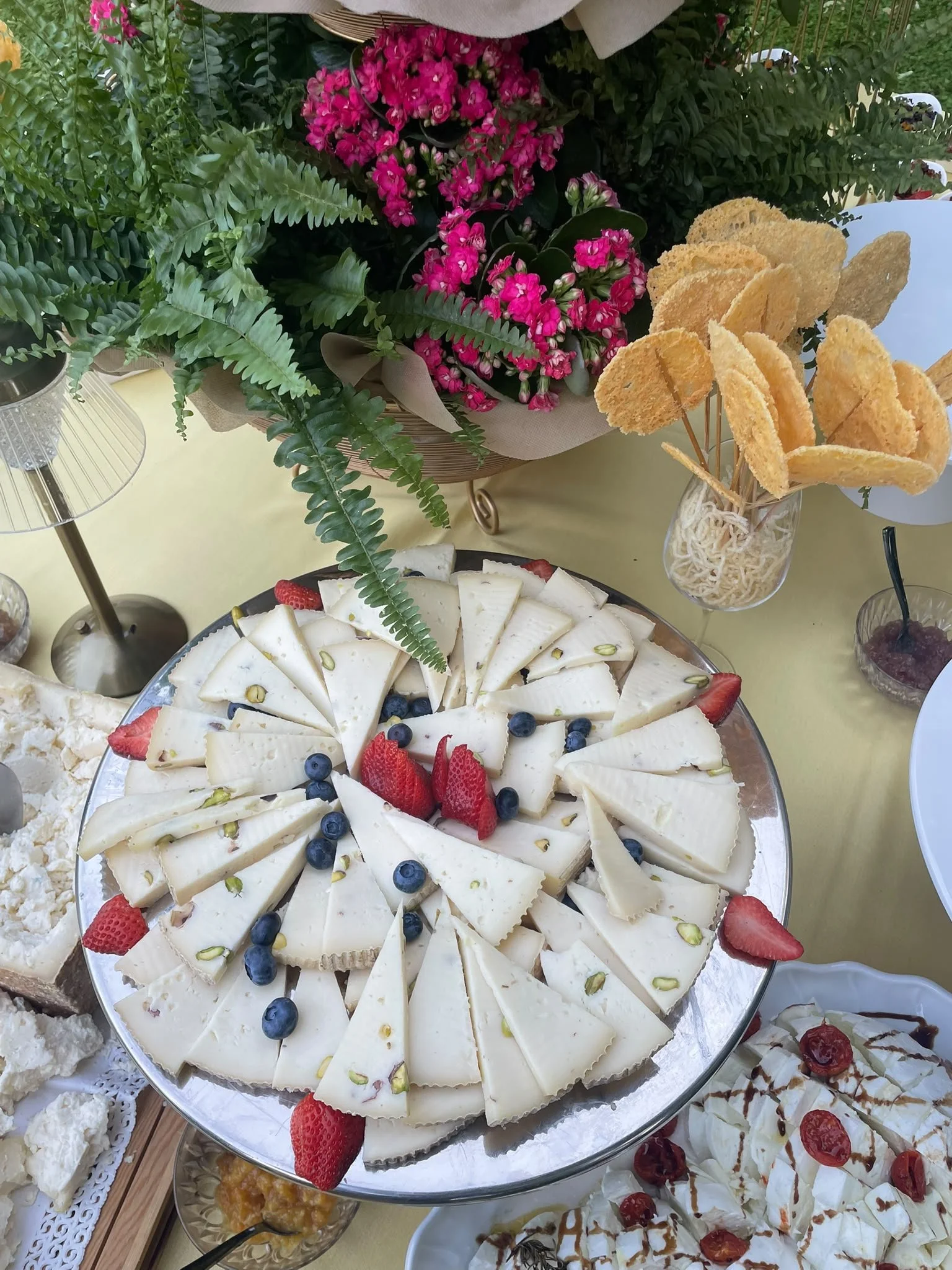Vassoio di formaggi decorati con fragole, mirtilli e pistacchi, lollipop di cialde di formaggio posizionati su un tavolo decorato con bouquet di fiori rosa e foglie verdi sul tavolo.