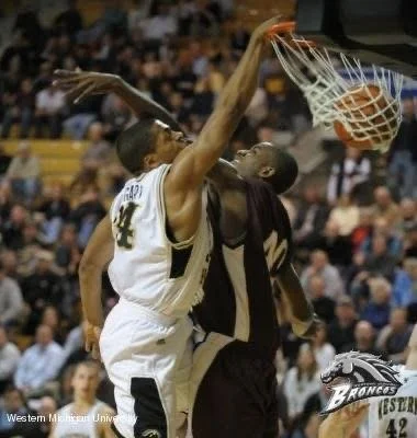 Basketball players competing during a game as spectators watch from the stands.