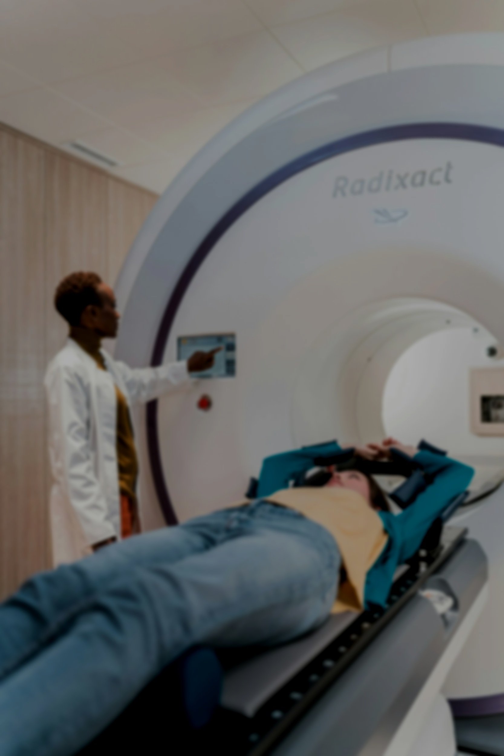 A person lying on a medical scanner bed during a scan, with a medical technician operating the scanner and pointing at a screen.