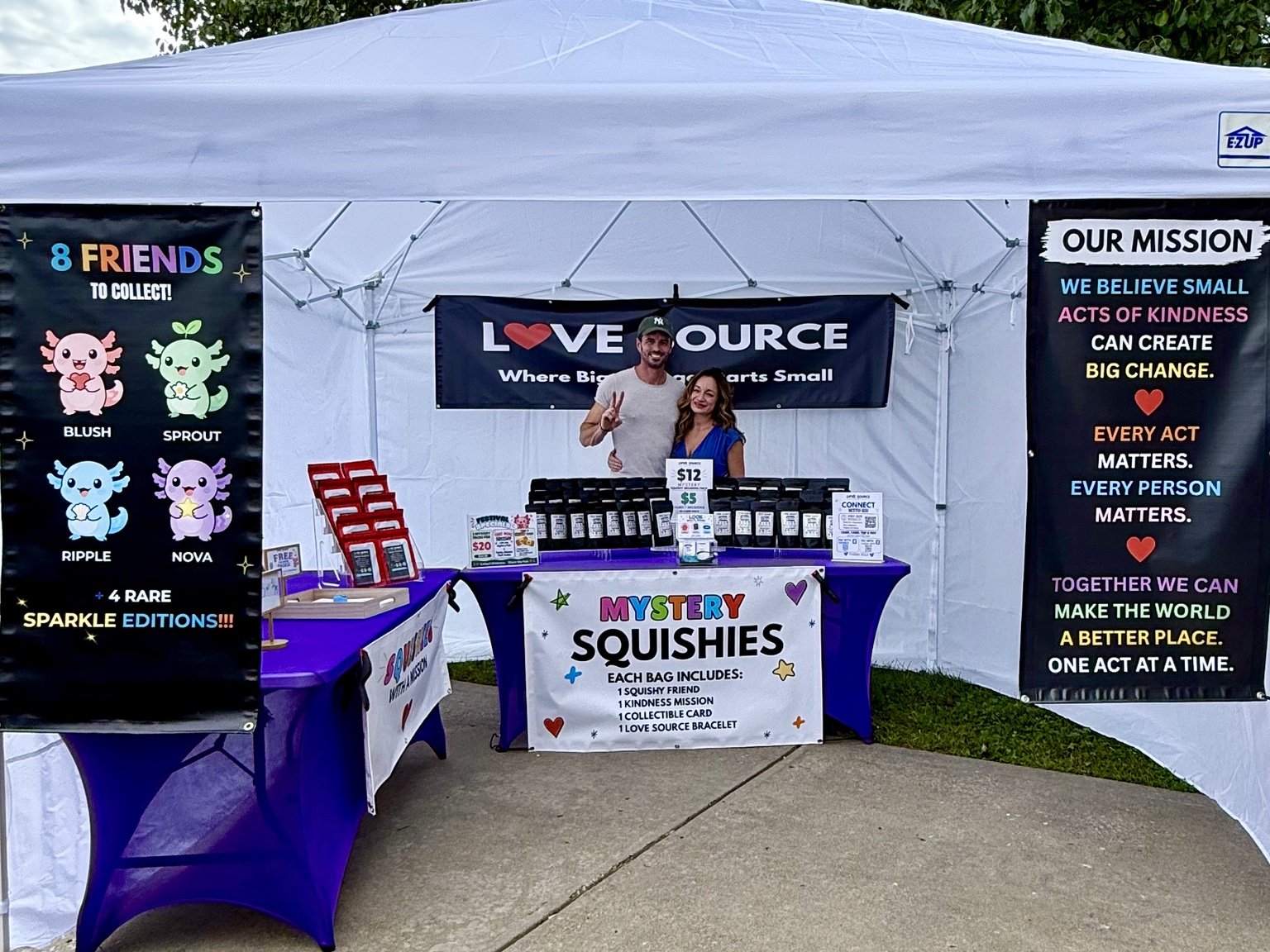 Two people standing together at the Love Source booth with mystery squishy bags and kindness mission displays.