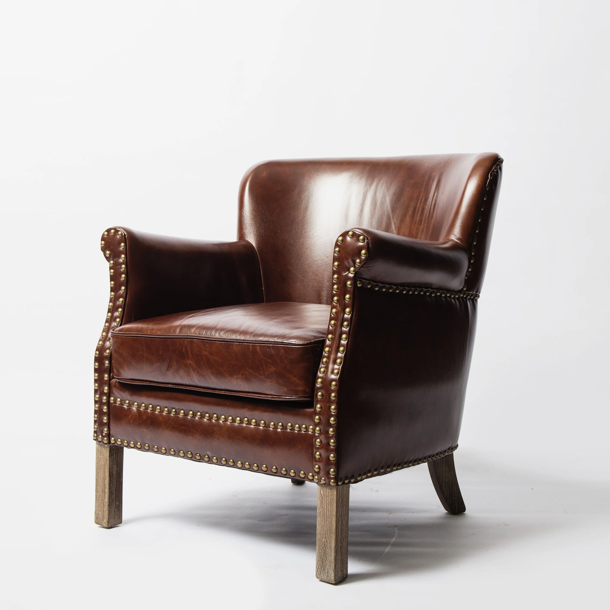 Brown leather armchair with nailhead trim on a light studio background.