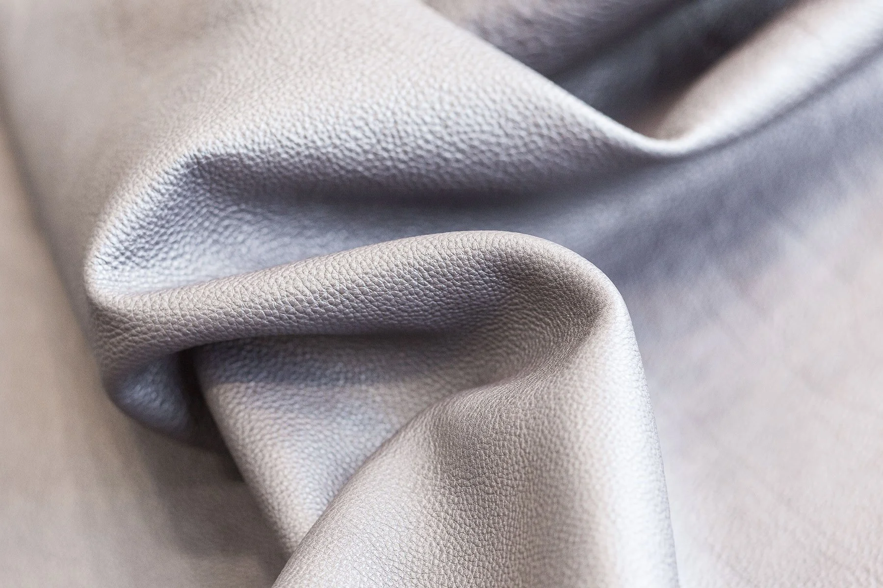 Close-up of light gray leather with soft folds and a subtle textured grain.