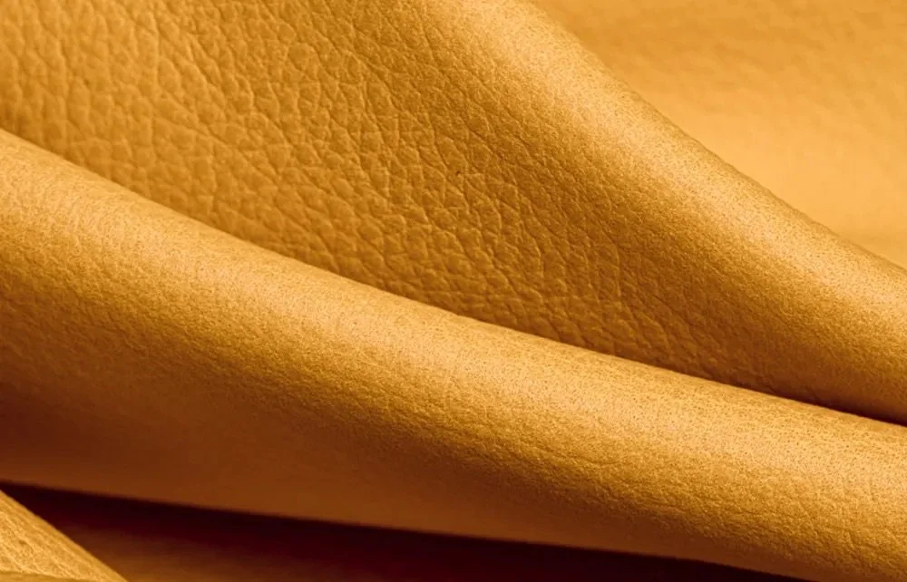 Close-up of tan leather showing natural grain, texture, and soft folds.