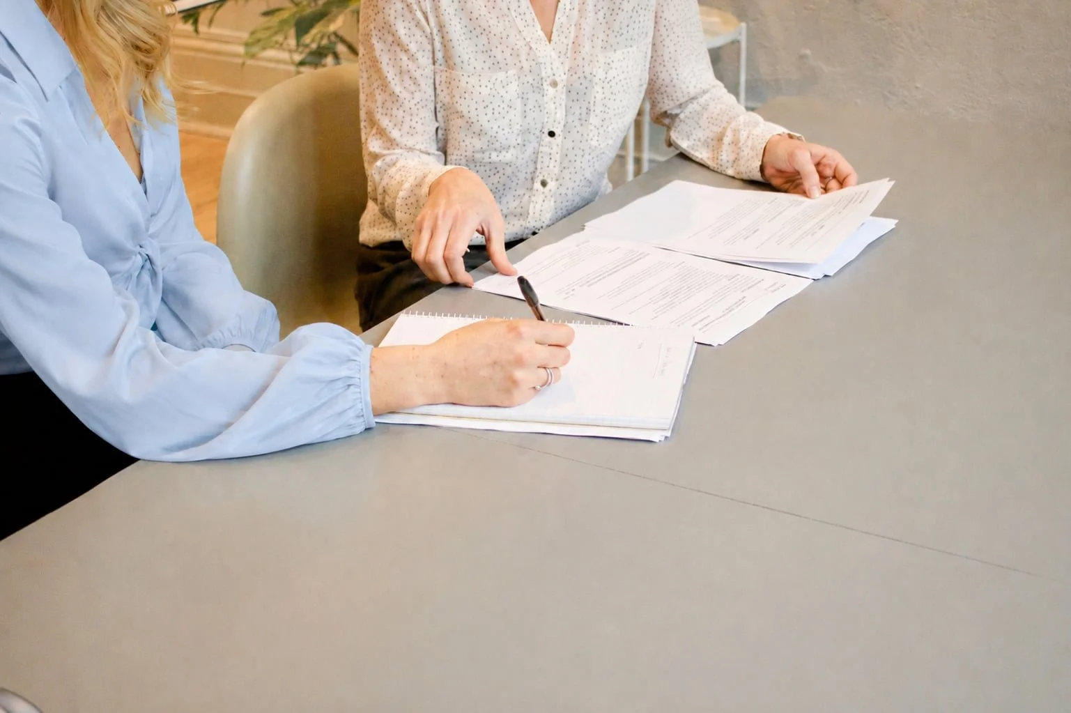 Two women sitting at a table reviewing and signing documents in an office setting.