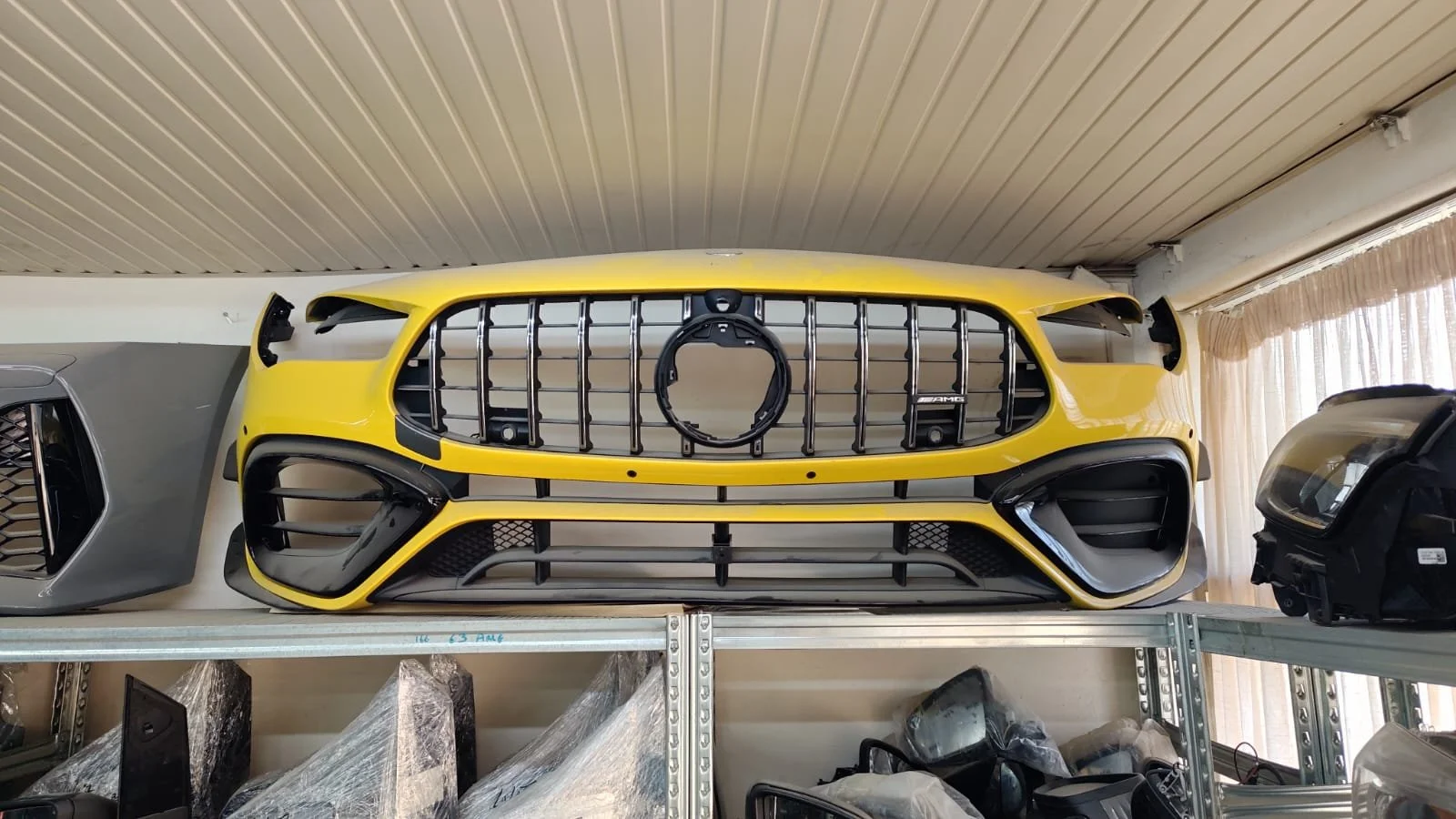Yellow Mercedes-Benz AMG car front grille and bumper on a shelf in a workshop.