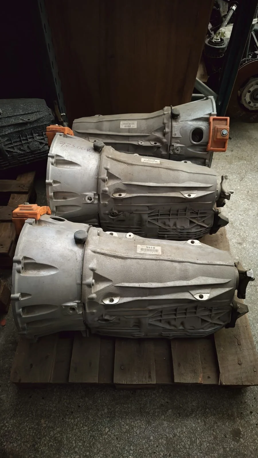 Three automotive transmissions placed on a wooden pallet in a garage or workshop.