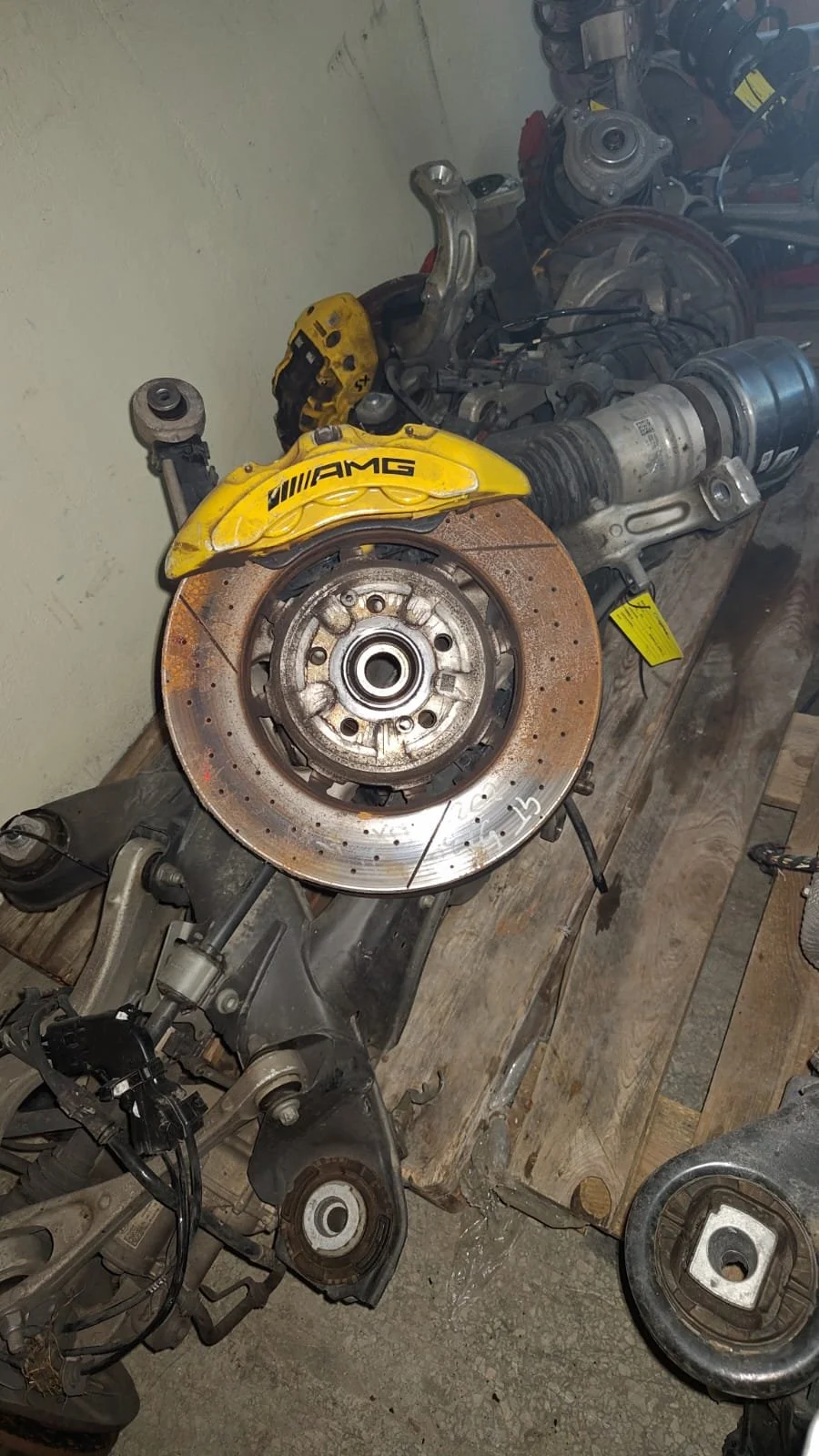 Disassembled car suspension components, brake disc, and AMG brake caliper, all placed on a workbench in a workshop.