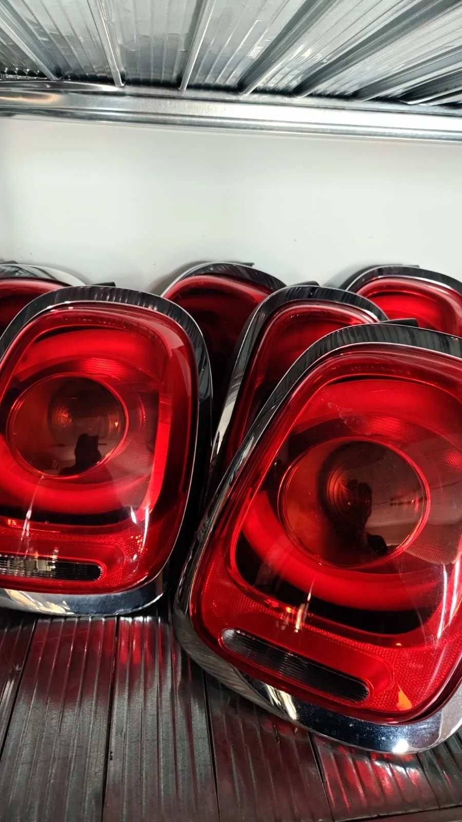 A close-up of multiple red tail lights stacked together on a metal surface, likely in a store or warehouse.