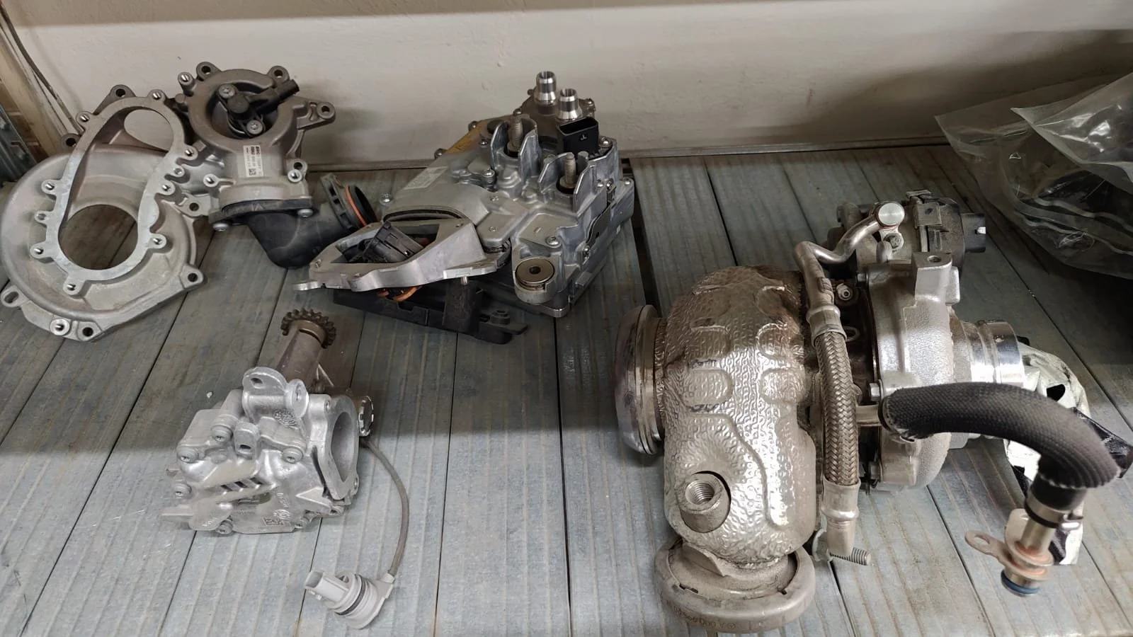 Various automotive engine components laid out on a wooden surface, including turbochargers and cylinder heads.