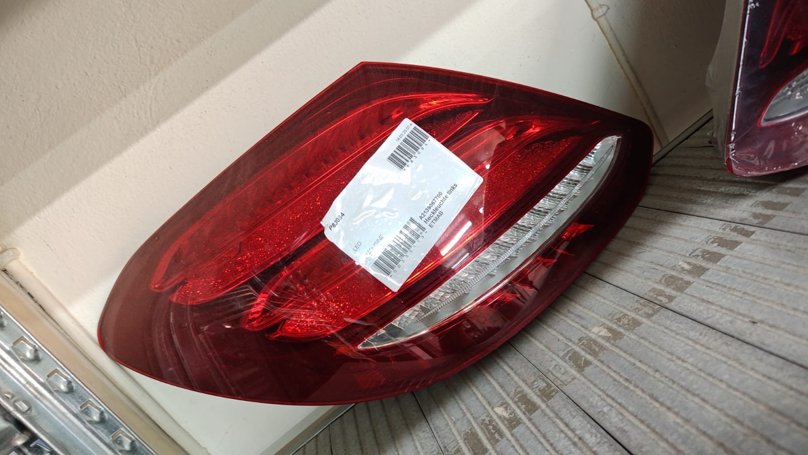 Red car tail light with a white shipping label on it, placed on a wooden surface next to a beige wall.